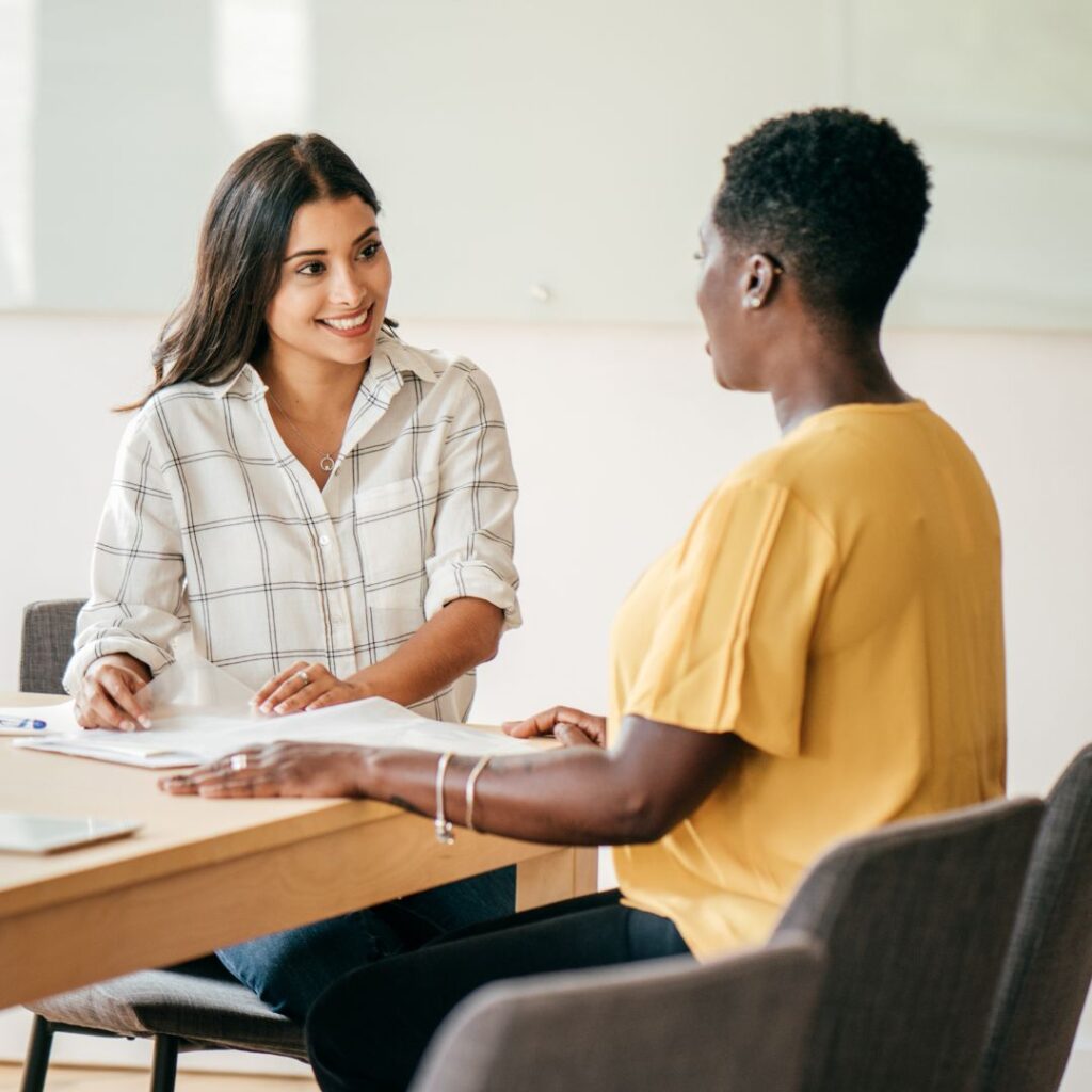 two woman talking to each other at a desk